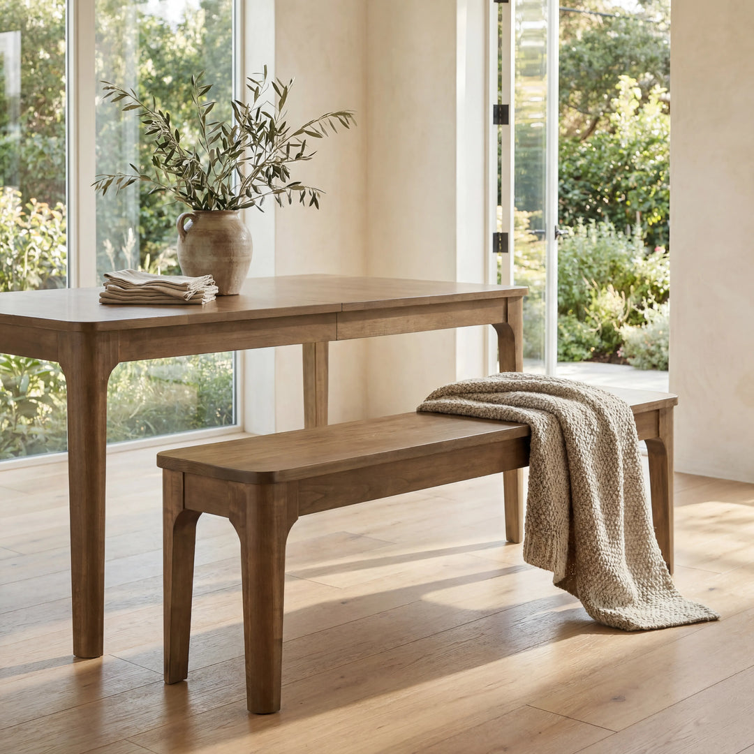 Wooden dining table with a bench and a vase of plants in a bright room.