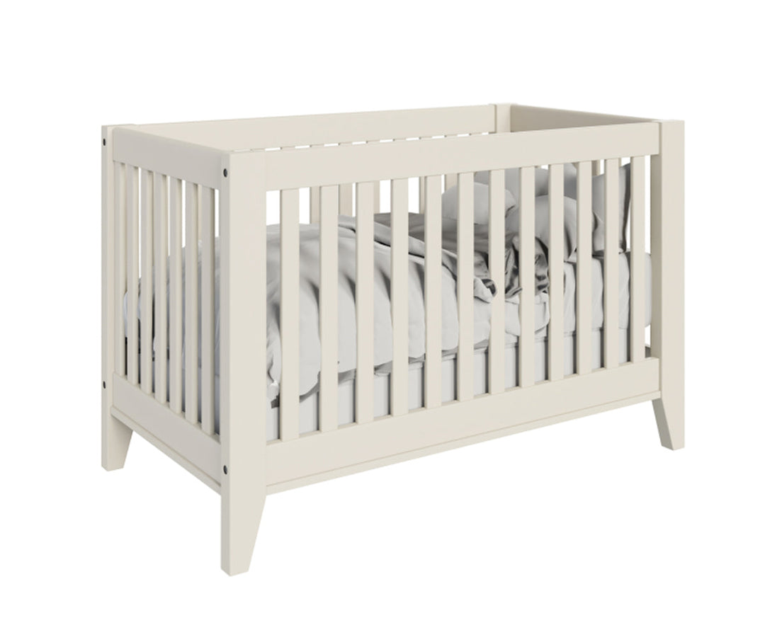 A white Newport crib with wooden panels and a shadow finish, featuring a fitted sheet and a pair of decorative bronze connector bolts.