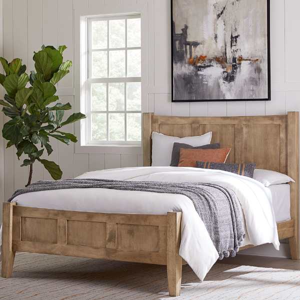 A Queen-sized bed with a wooden headboard and footboard, made from Brown Maple with Sandstone stain, arranged in a bedroom setting with bedding and a wall painting.
