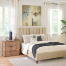 Neatly made bed with beige headboard and matching nightstand in a bright bedroom.