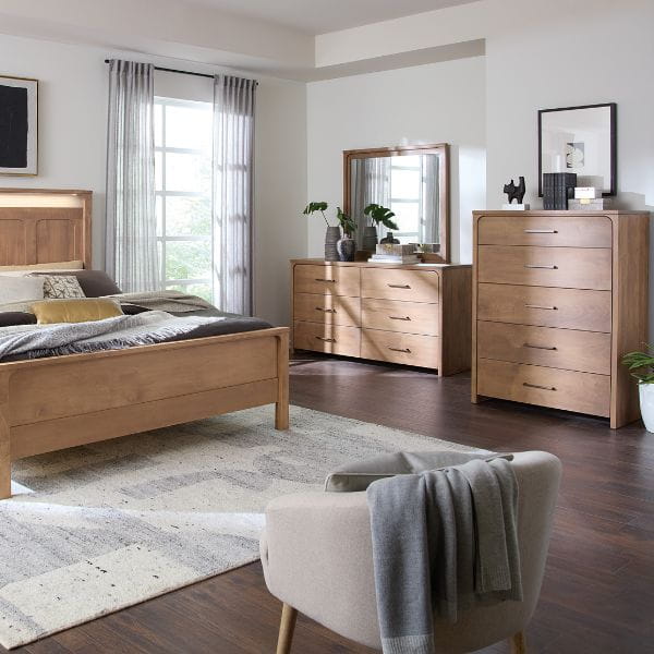 Wooden bedroom furniture including a bed, dresser, and chair in a well-lit room.