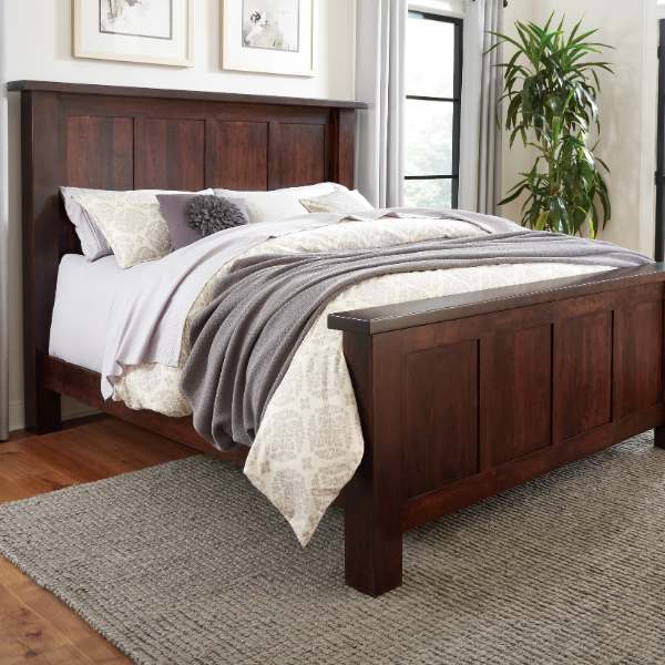 A contemporary style bed with a dark wood headboard and footboard, made in a room with a light decor.