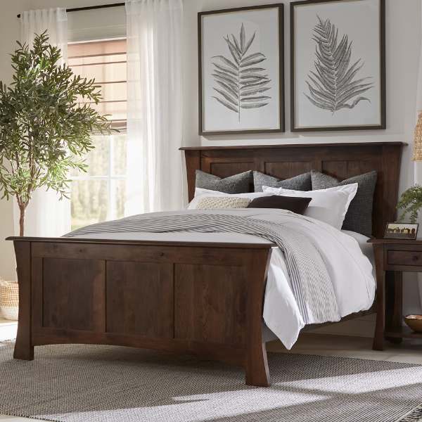 A contemporary style bedroom set with a brown headboard and footboard, made from rustic hickory, with a white comforter and gray pillows. The set includes a nightstand and the room has a bright, clean aesthetic with a large window and minimalist decor.