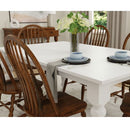 Dining room with a white table and wooden chairs, set for a meal.