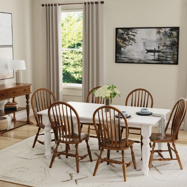 Dining room with wooden chairs around a white table, light-colored walls, and large windows.