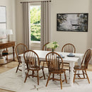Dining room with wooden chairs around a white table, light-colored walls, and large windows.