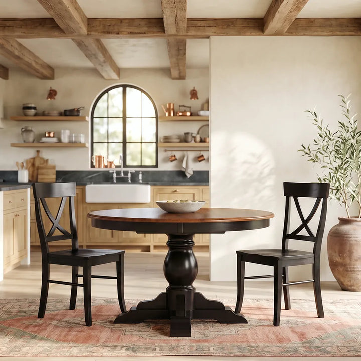 Amish Albany Round Pedestal Dining Table with a two-tone stain, paired with black Carmen X-back dining chairs in a farmhouse kitchen space featuring exposed wood beams and arched windows.