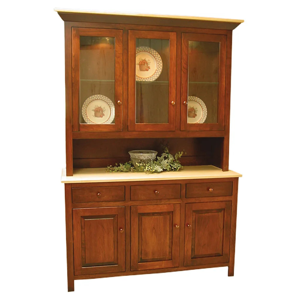 A mid-century wooden hutch and sideboard cabinet with a warm medium-brown finish, featuring three upper glass-front doors with decorative plates, a central open shelf with greenery and a bowl, and three lower cabinet doors with drawers above. The cabinet has a light beige stone or laminate top and bottom surfaces.
