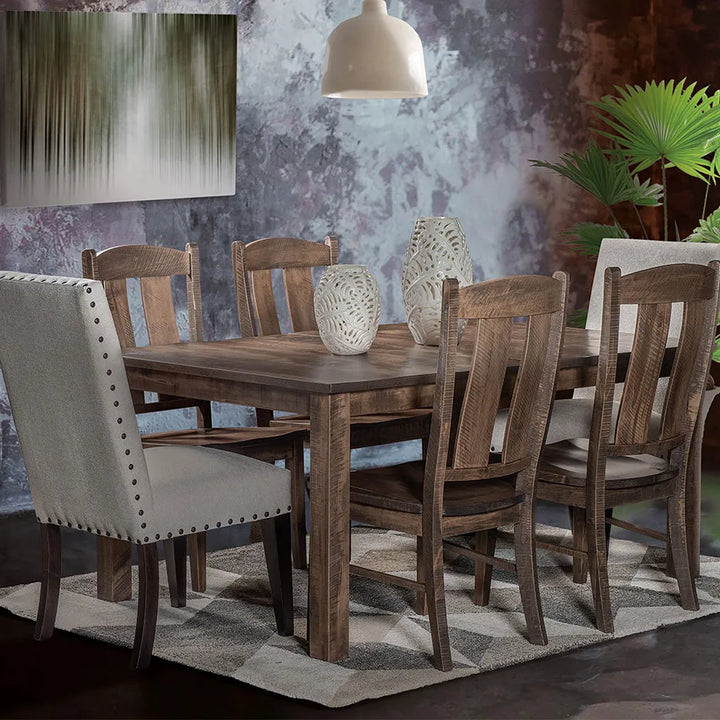 A rustic wooden dining table with six matching wooden chairs, styled in a dining room setting with a patterned rug, a hanging pendant light, and a textured wall.