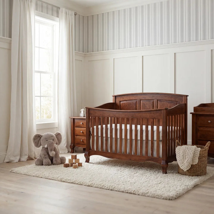 A dark brown wooden crib with a guard rail is shown in a styled nursery setting with a matching wooden nightstand, a plush elephant toy, a shag rug, and striped wallpaper.