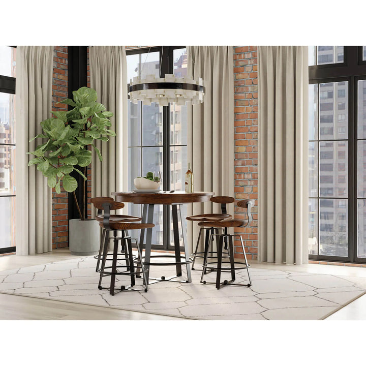 A 5-piece pub height dining set featuring a round dark wood table and four matching bar stools with dark metal frames, set in a modern loft-style room with brick walls, large windows, and beige curtains.