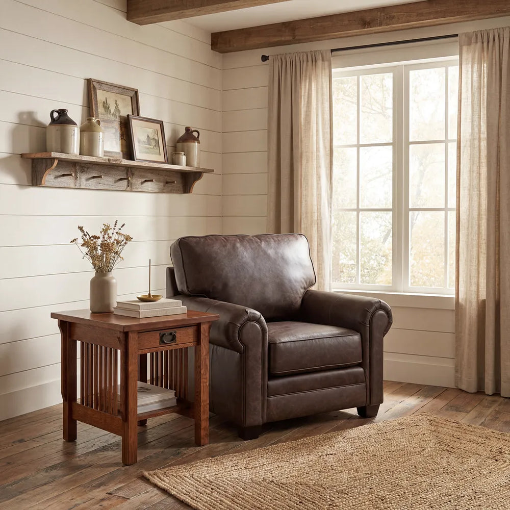 A rustic brown leather armchair in a cozy, sunlit room with white shiplap walls, a wooden side table, and a large window with beige curtains.
