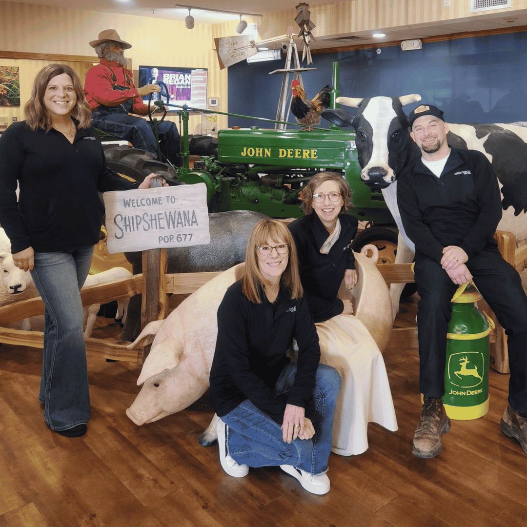 Group of people with farm animals and a John Deere tractor in a room.