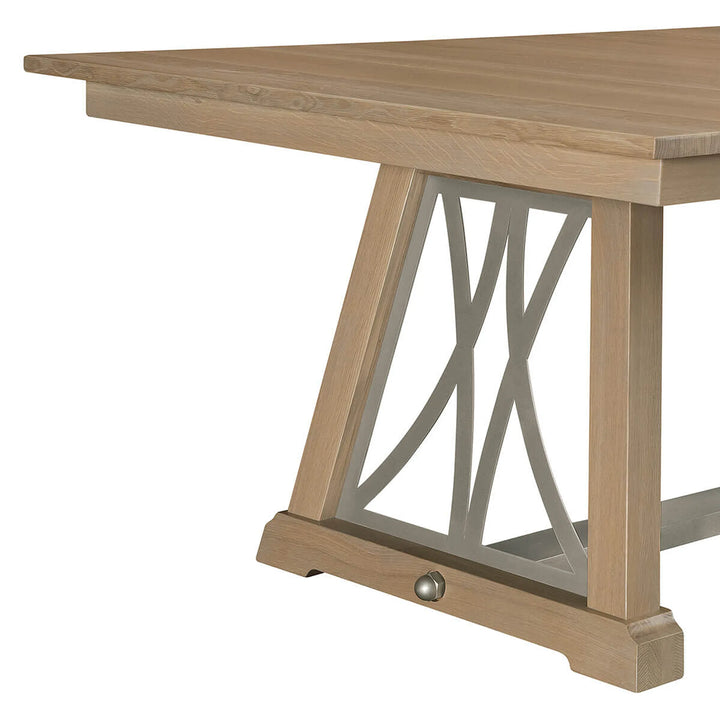 Close-up of a light oak dining table showing the trestle base with a silver metal X-shaped support and a small round metal knob.