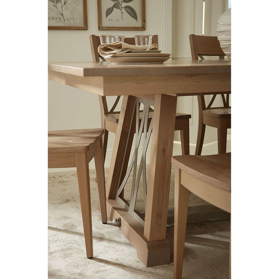 A light natural wood dining table with matching wooden chairs, shown in a styled dining room setting with neutral decor and framed wall art.