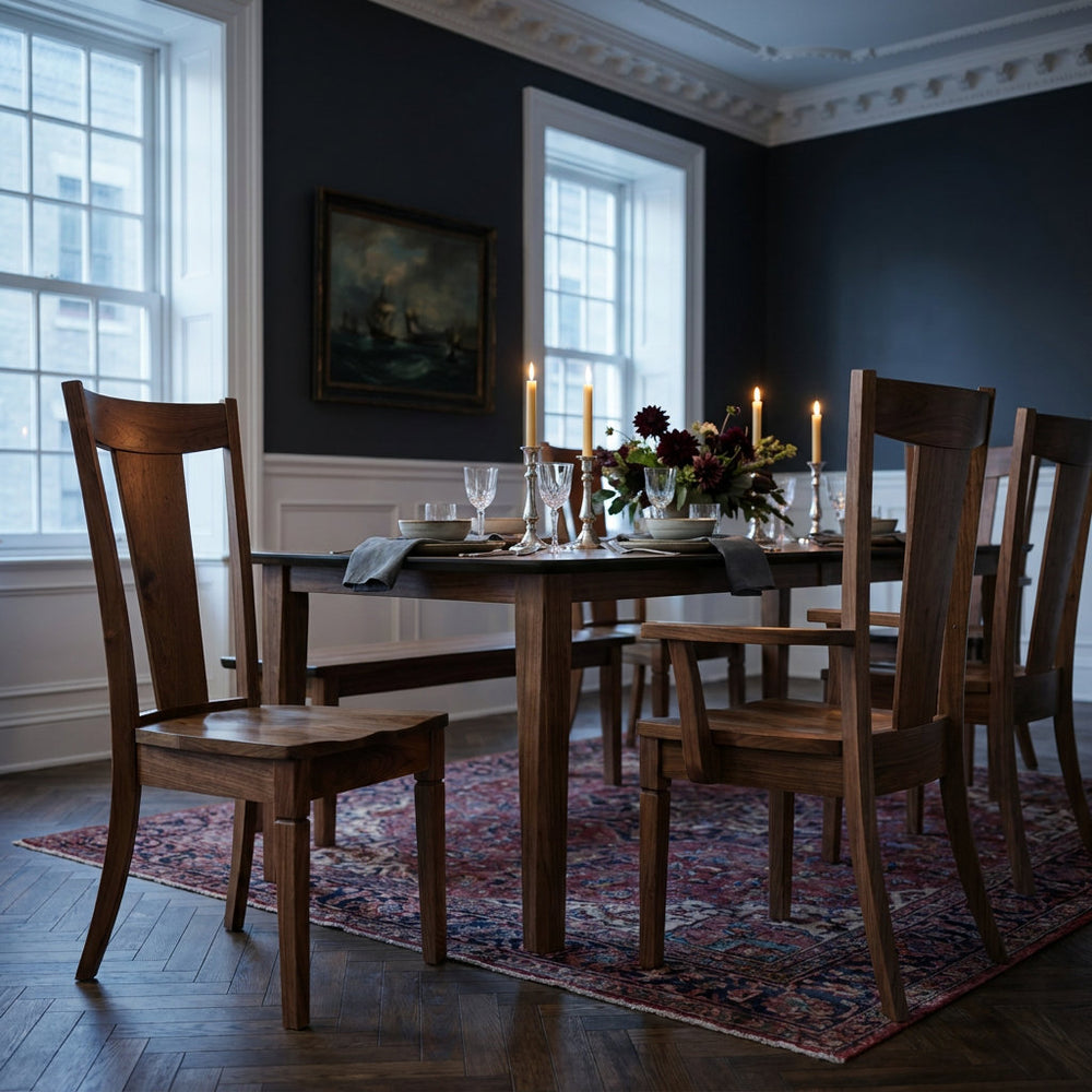 A dark wood dining table and matching wooden chairs arranged on a patterned area rug in a dimly lit dining room with dark blue walls, white trim, and lit candles on the table.