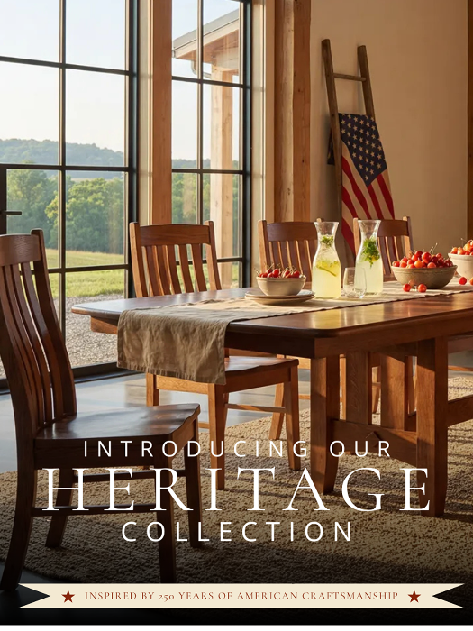 A dining room scene with a wooden table and matching chairs, set with a table runner, pitchers, bowls of fruit, and an American flag leaning against the wall. Large text across the lower portion reads 'INTRODUCING OUR HERITAGE COLLECTION' with a banner at the bottom reading 'INSPIRED BY 250 YEARS OF AMERICAN CRAFTSMANSHIP.