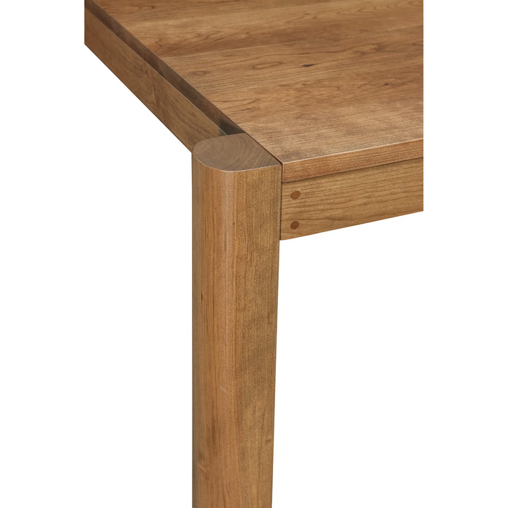 Close-up of a wooden table corner showing the tabletop and thick round leg with visible wood grain and joinery on a white background.