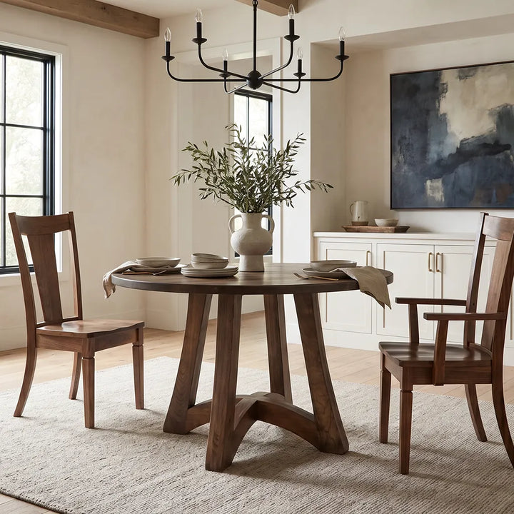 Tifton Solid Top Pedestal Dining Table in a warm wood finish, featuring a distinctive angled pedestal base, paired with wooden dining chairs in a bright, modern farmhouse dining room.