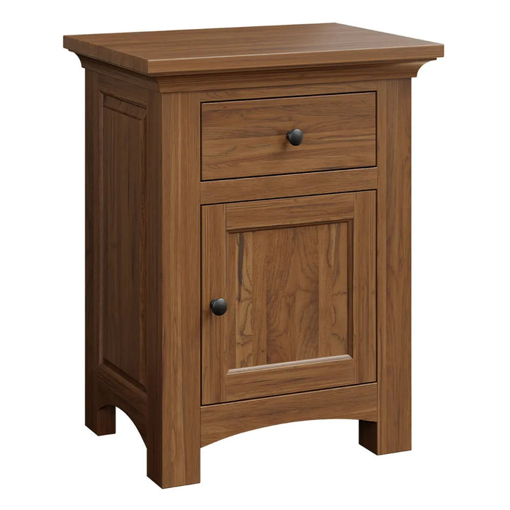 A small wooden nightstand or end table with a medium brown finish, featuring a single drawer on top and a cabinet door below, both with round black knobs, shown on a plain white background.