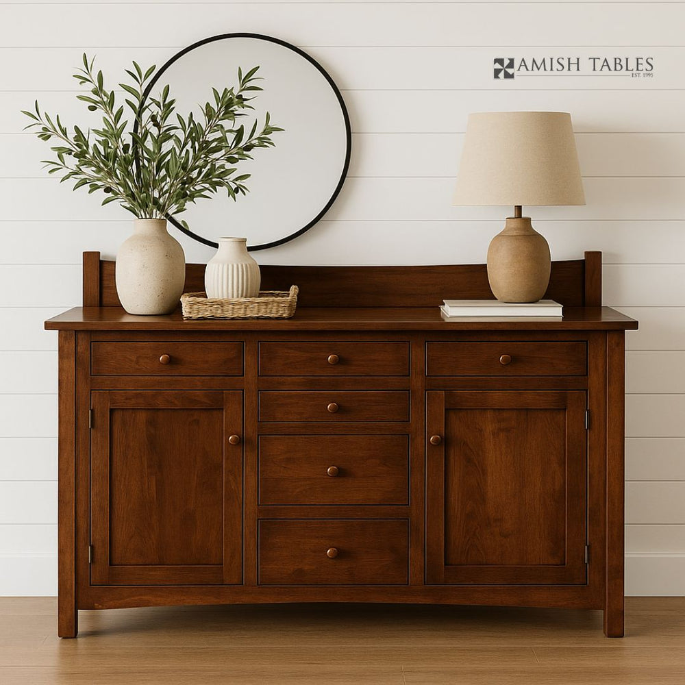 Wooden sideboard with decorative items against a white wall, featuring the Amish Tables logo.