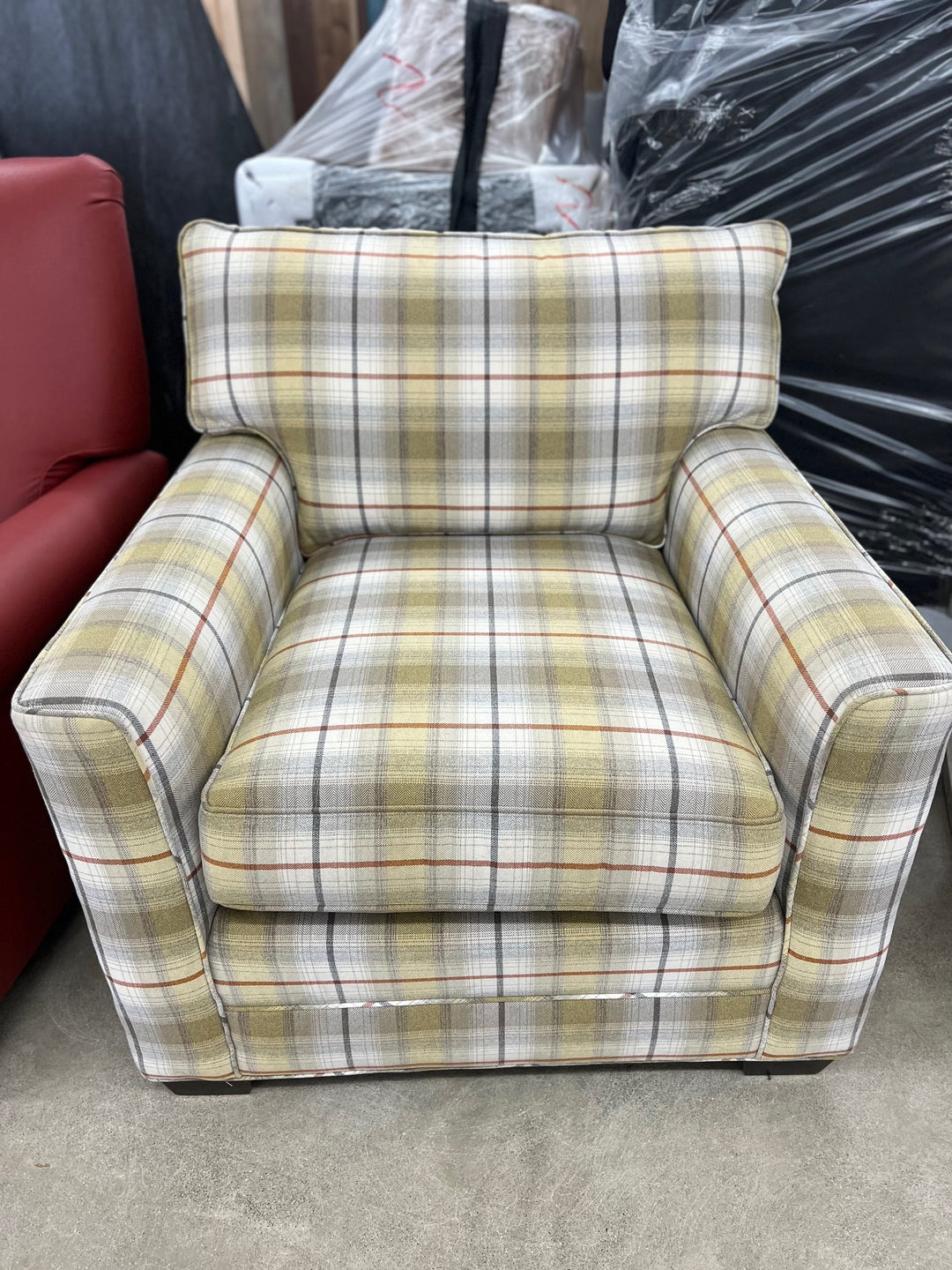 A showroom model chair with a plaid pattern, featuring a beige cushioned seat and backrest, and a patterned fabric on the arms.