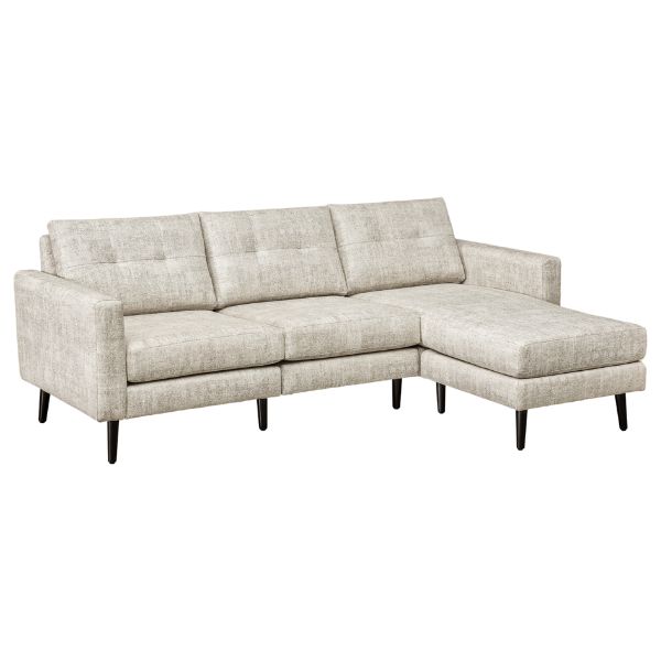 A well-lit living room featuring a beige upholstered sofa set with a design that includes mission lines, alongside a matching armchair and footstool, set on a patterned rug.